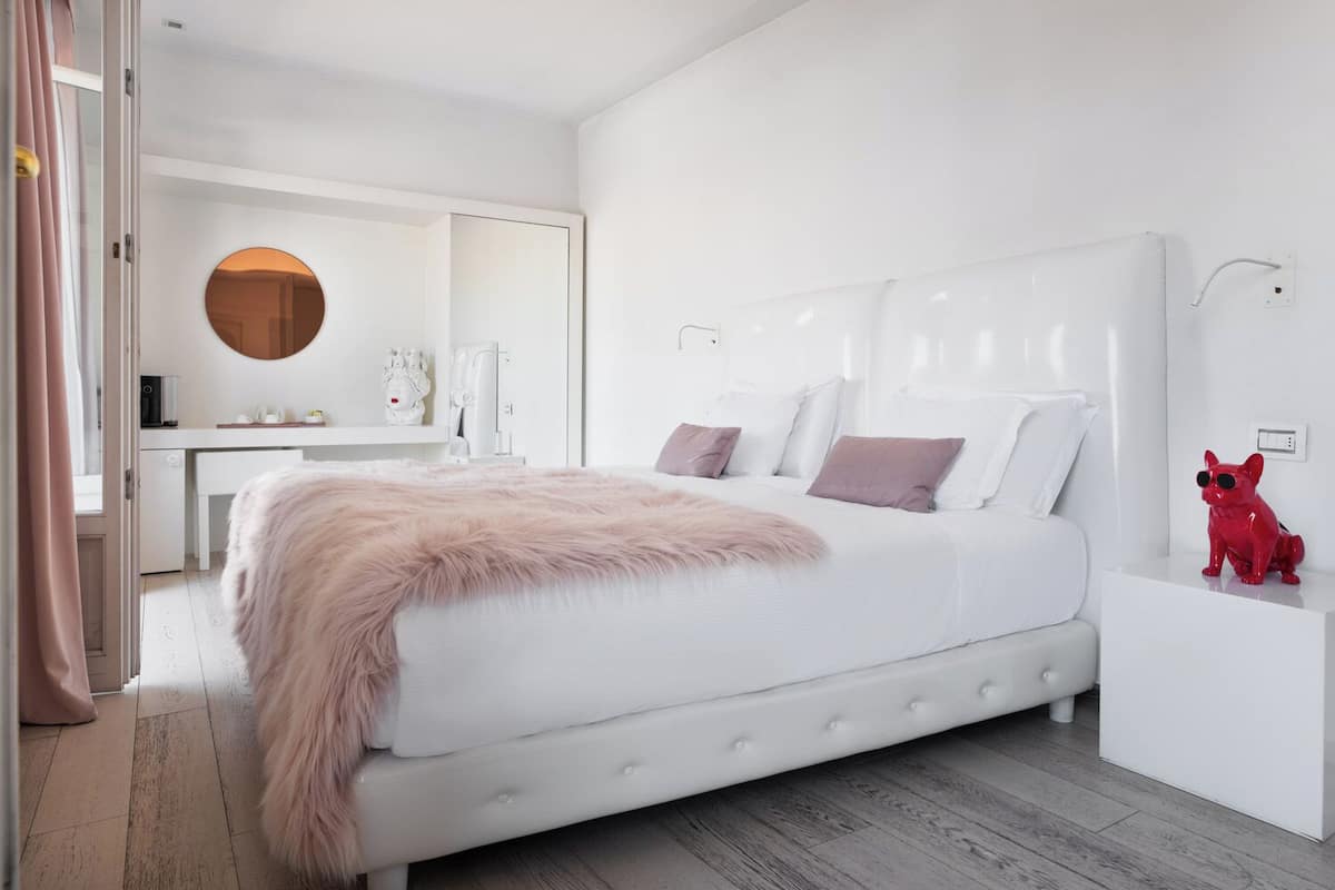 A modern bedroom with a large bed, a bedside table, a red dog figurine, and a round mirror on the wall.