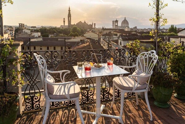 A balcony with two white chairs and a table set for two, overlooking a cityscape with historic buildings.