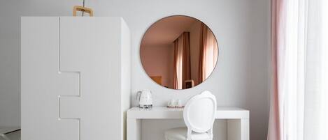Una habitación minimalista con un escritorio blanco, una silla, un espejo redondo y un armario.