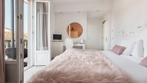 A modern hotel room with a large bed, a round mirror, a desk, and a view of the outdoors.