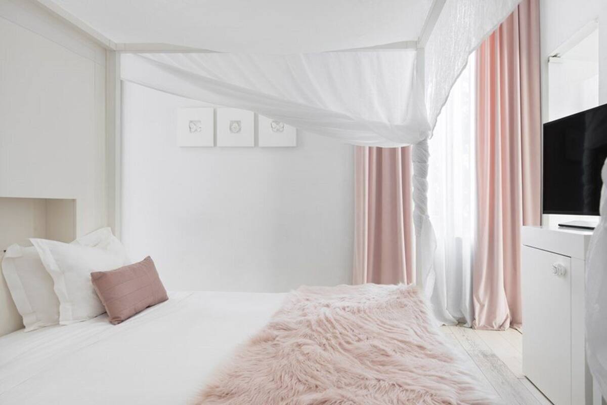 A bedroom with a bed, a fluffy rug, a TV, and curtains.