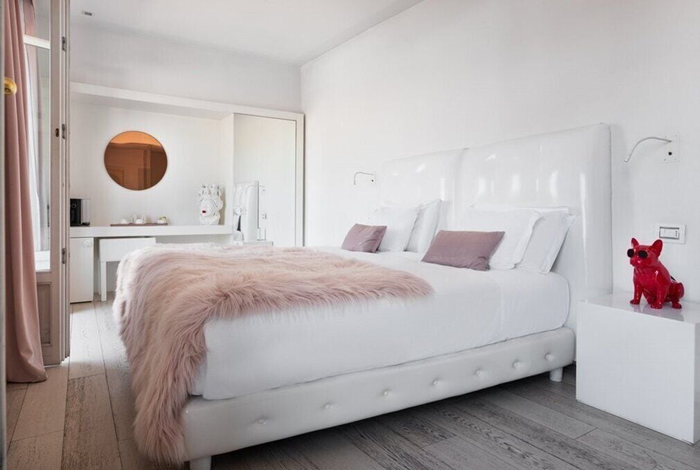 Une chambre à coucher moderne avec un grand lit, une commode blanche, un miroir rond et une statuette de chien rouge.