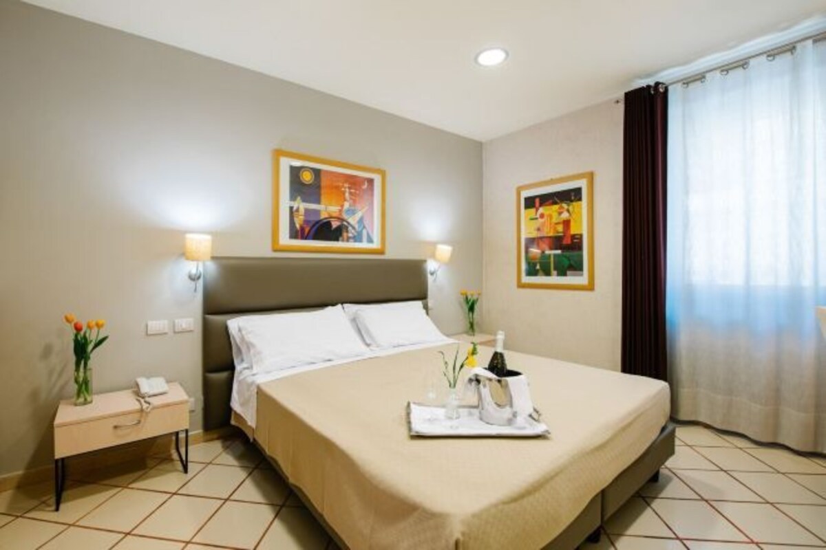 Una habitación de hotel con cama, mesitas de noche y obras de arte en las paredes.