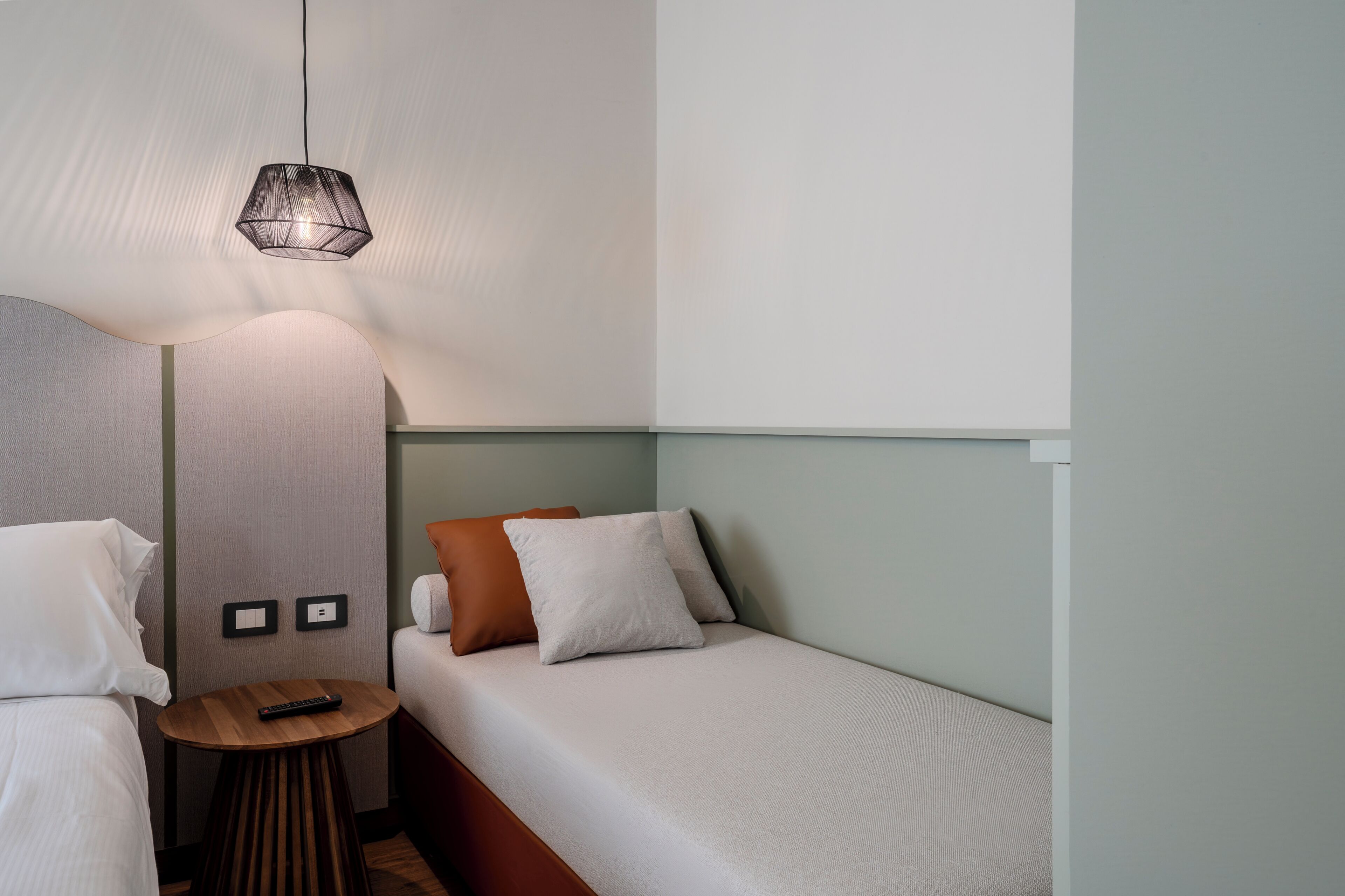 Een hotelkamer met een bed, een nachtkastje, een lamp en een bedieningspaneel aan de muur.