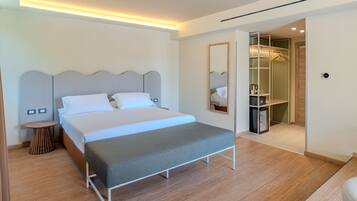Una habitación de hotel moderna con una cama grande, mesitas de noche, un espejo y un vestidor.