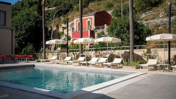 Una piscina al aire libre, sombrillas, sillones reclinables de piscina