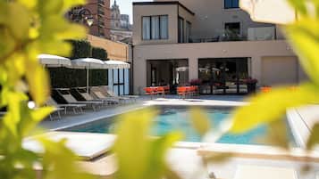 Una piscina al aire libre, sombrillas, sillones reclinables de piscina