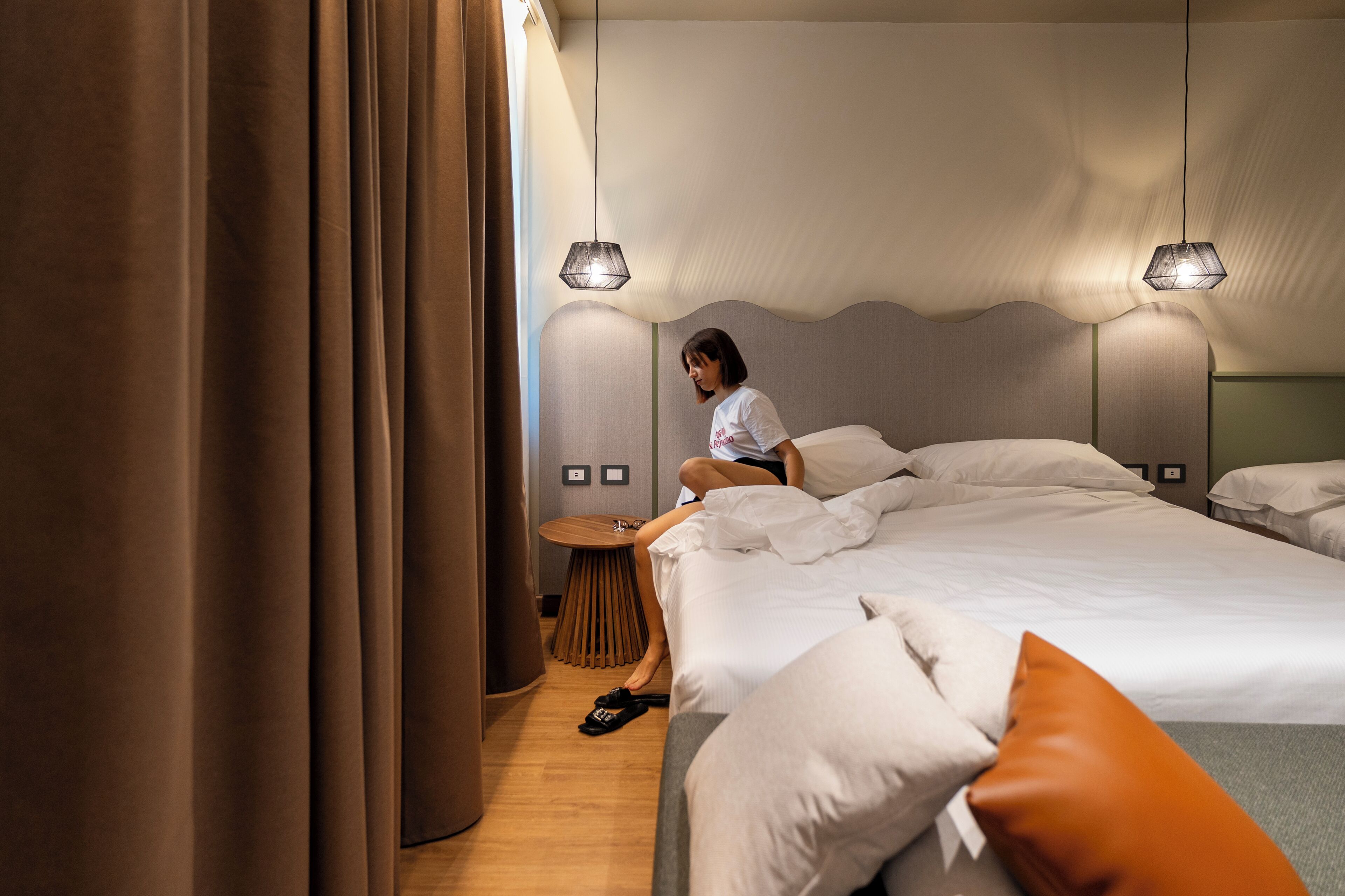 A hotel room with a large bed, a round wooden table, and two wall-mounted lamps.