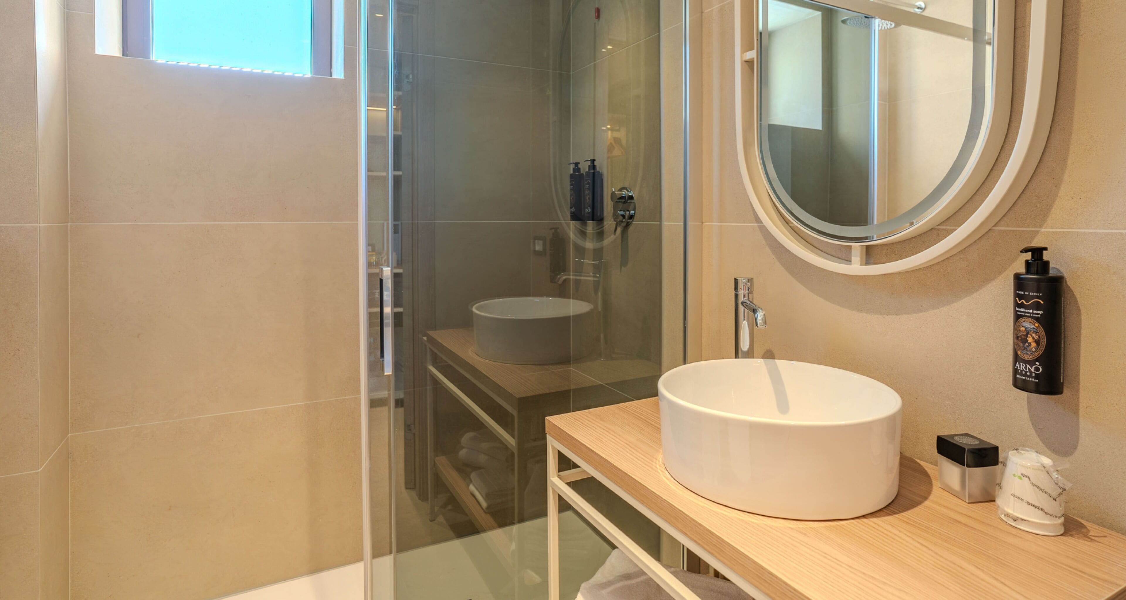Un baño moderno con cabina de ducha de vidrio, un espejo redondo y un lavabo blanco sobre una encimera de madera.