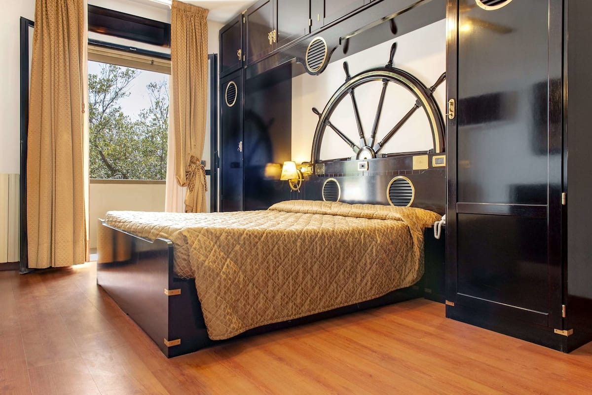 Un dormitorio moderno con cama, un ventanal grande y un diseño de pared único con una rueda de barco.