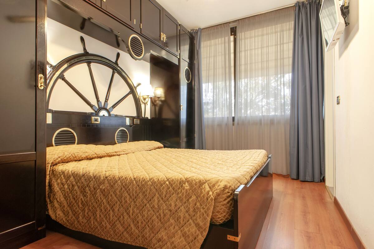 Una habitación con cama, un cabecero grande con forma de rueda y una ventana con cortinas.