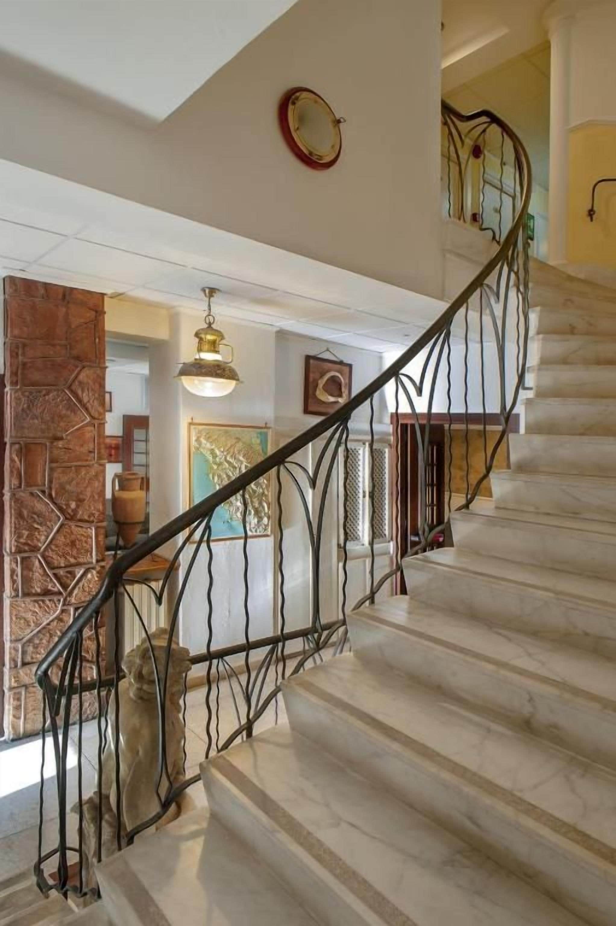 Una escalera con barandilla de metal, una pared con diseño geométrico y una lámpara colgante.