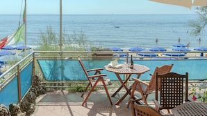Zona junto a la piscina con mesa y sillas, una bandera y vistas al mar.