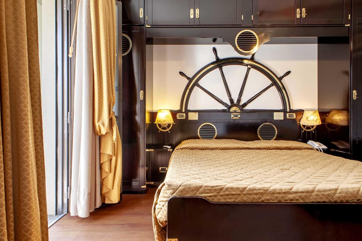 Un dormitorio con una cama grande, cabecero de madera oscura con un timón de barco y dos apliques de pared.