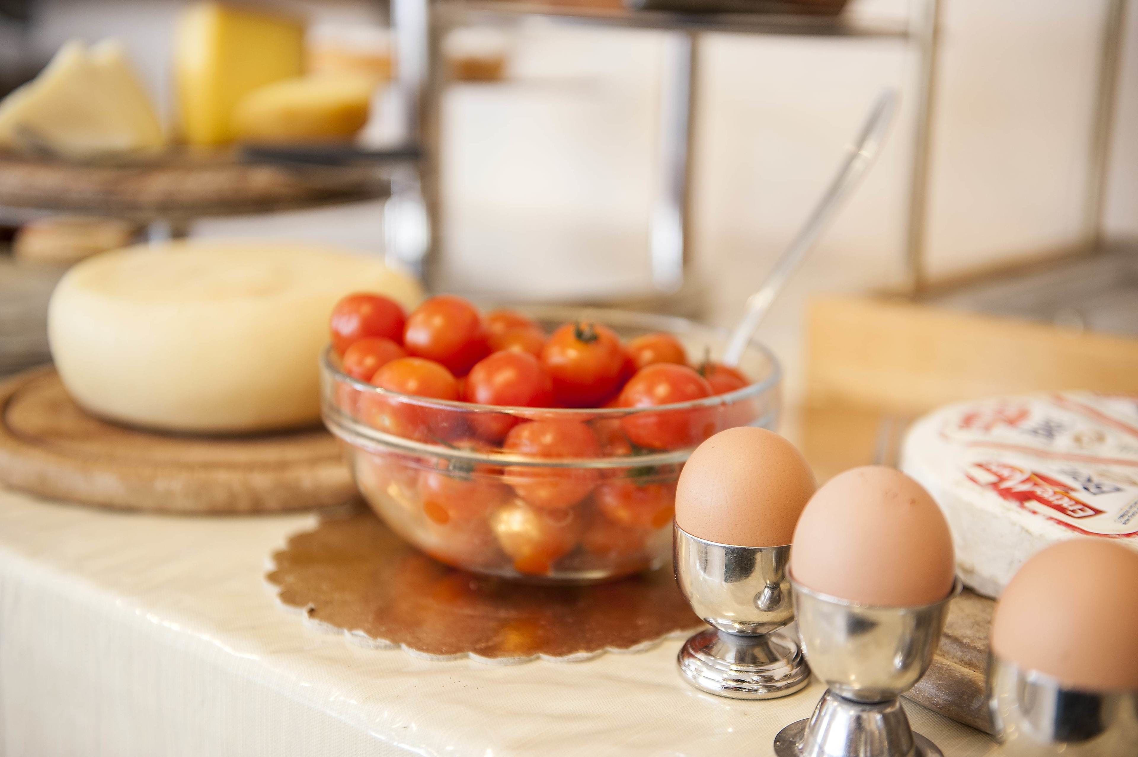 Uma bancada de cozinha com uma tigela de tomate cereja, um bloco de queijo e dois ovos em recipientes de metal.