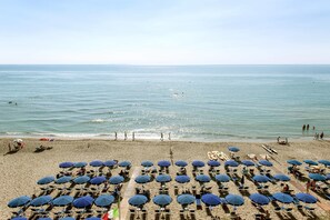 Ein Strand mit Reihen von Liegen und Sonnenschirmen, ein klarer Himmel und das Meer im Hintergrund.