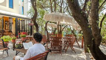 Un hombre leyendo en un banco en un área de estar al aire libre, con sombrillas y plantas en macetas.