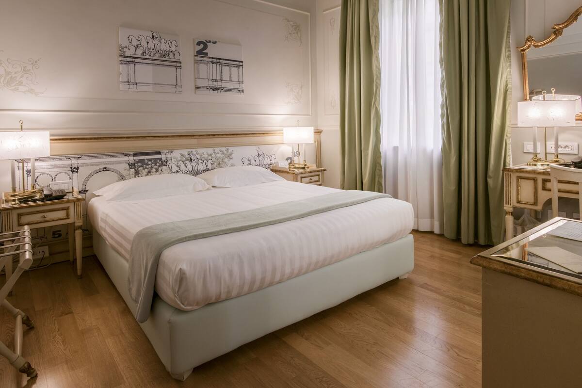 A neatly arranged hotel room with a large bed, bedside tables with lamps, a dresser, and a mirror.