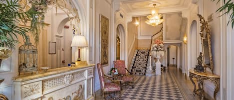 Un amplio pasillo con decoraciones elaboradas, piso a cuadros y una zona de recepción con un cartel que dice "RECEPTION".