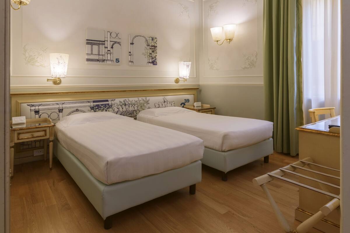 A hotel room with two beds, a nightstand with a phone, wall art, and a window with curtains.