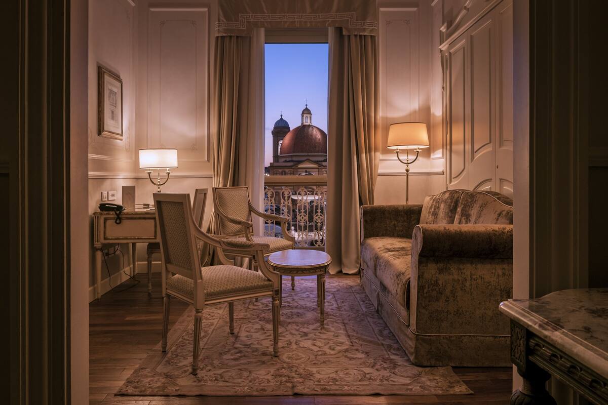 A room with a view of a domed building, a sofa, a chair, a small table, and a lamp.