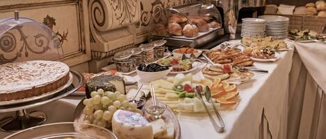 A buffet with various food items including cheese, fruits, and pastries.