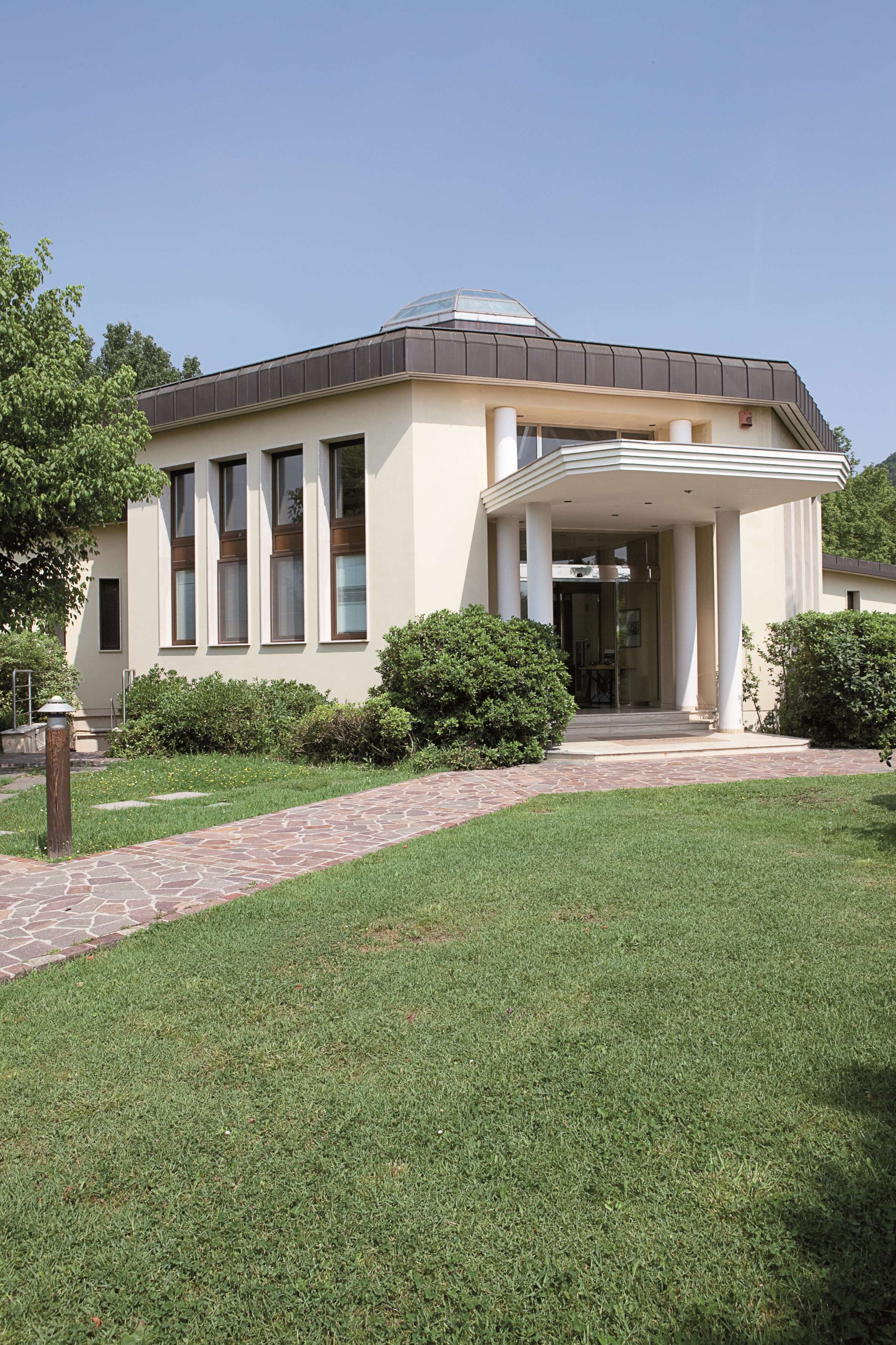 A modern building with a covered entrance, large windows, and a well-maintained lawn.