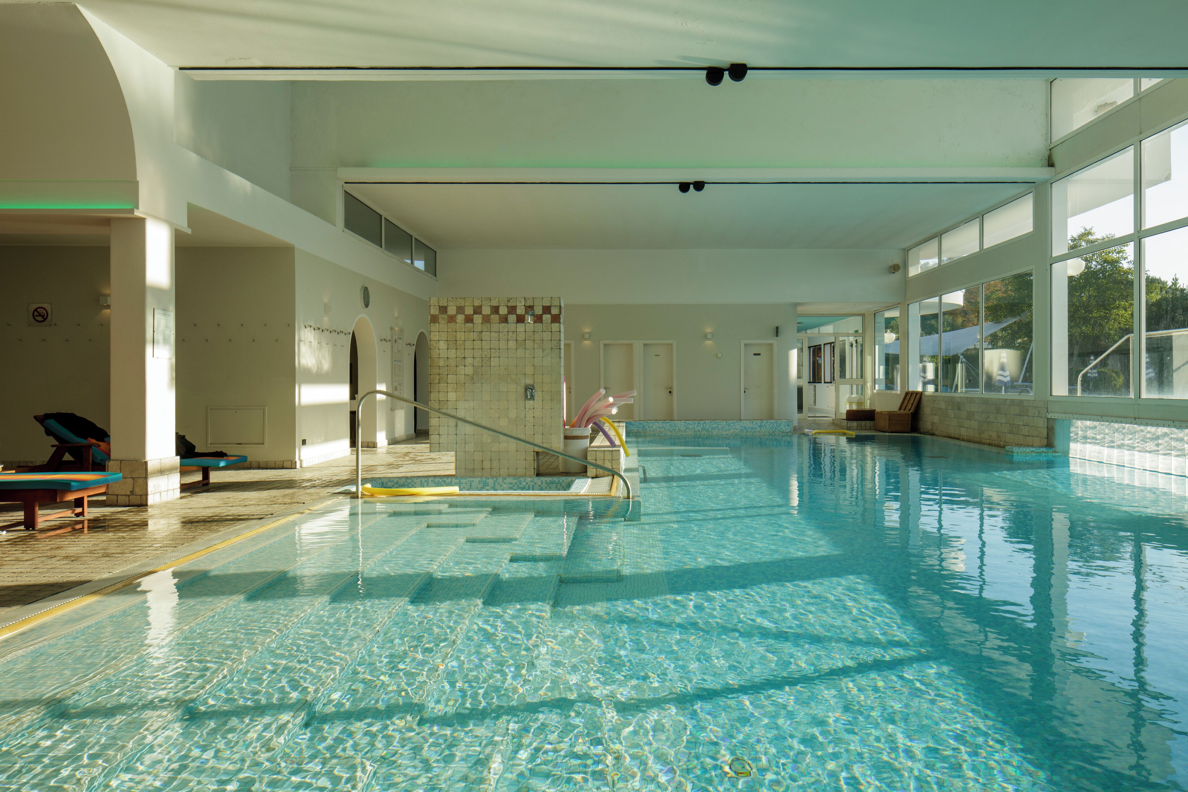 An indoor swimming pool with clear water, tiled walls, and a few lounge chairs.