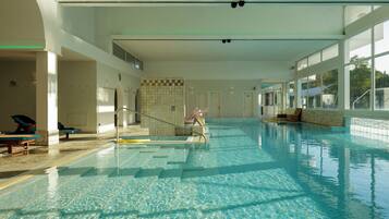 An indoor swimming pool with clear water, tiled walls, and a few lounge chairs.
