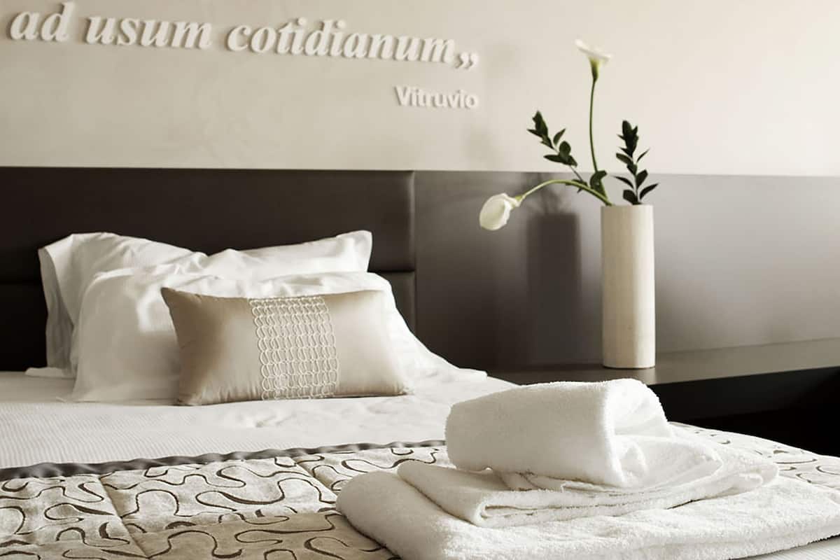 A modern hotel room with a bed, pillows, a vase with flowers, and a quote on the wall.
