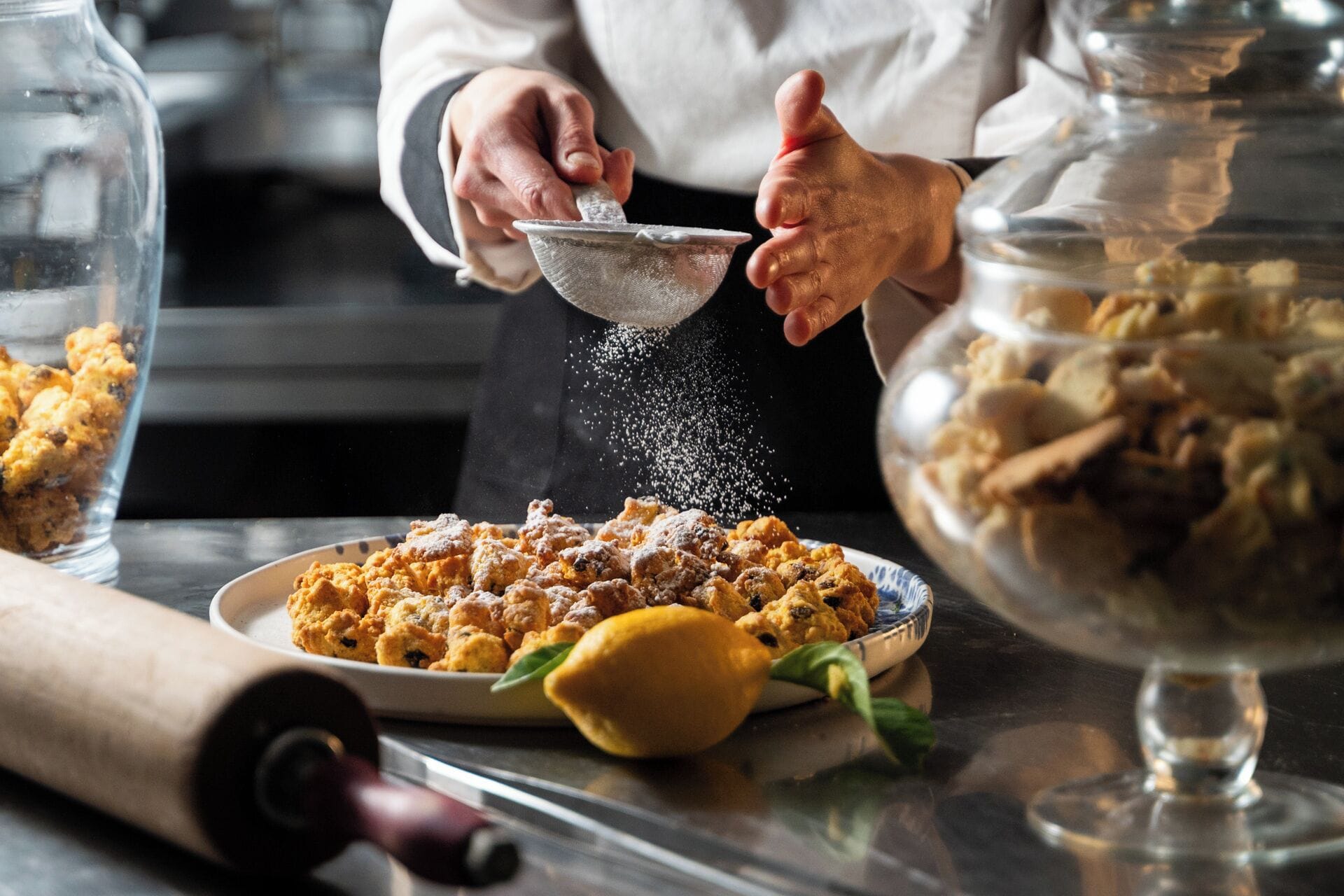 A person sprinkling powdered sugar over a dish of cookies.