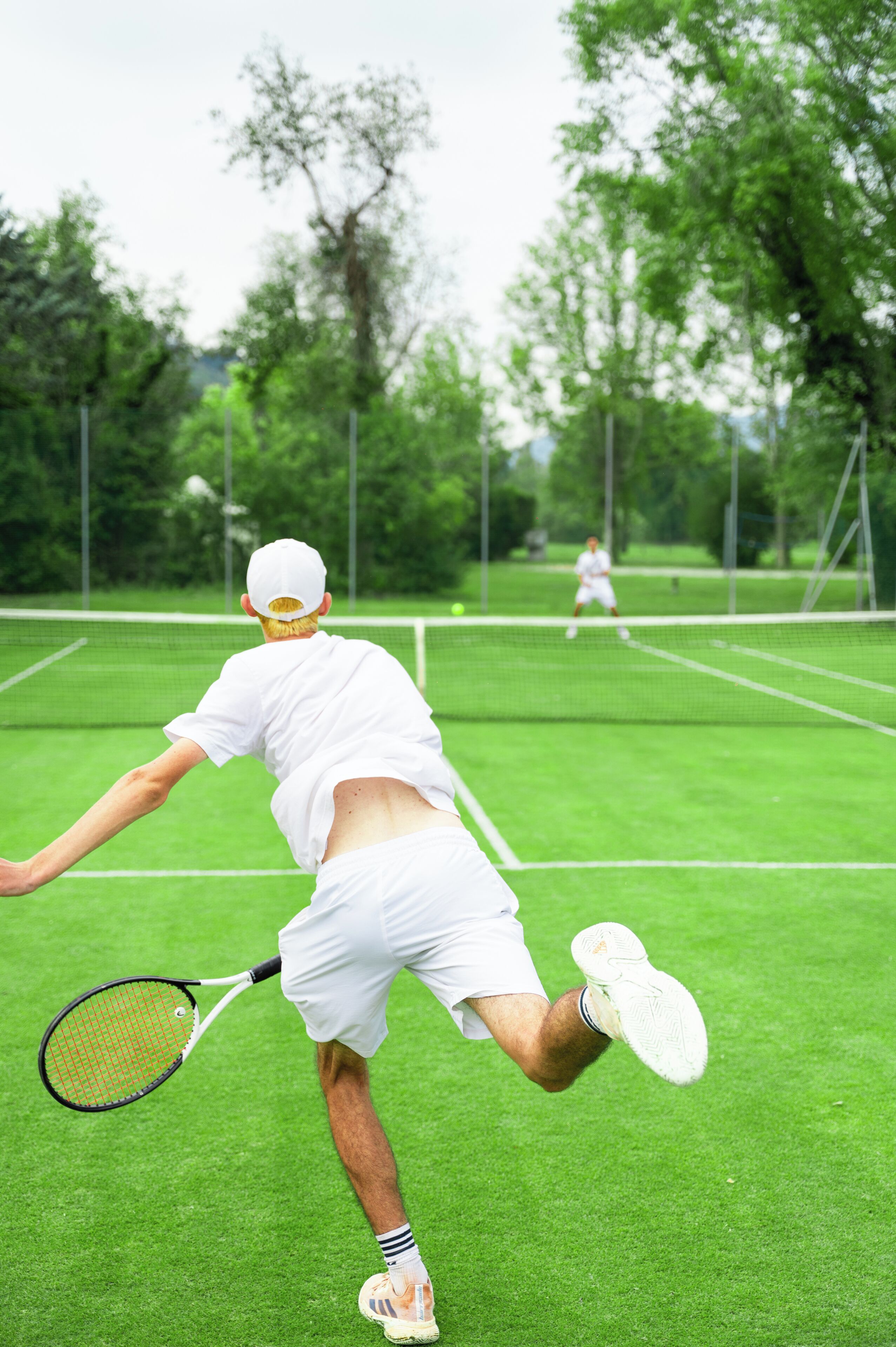 Un court de tennis avec un joueur en plein mouvement, un autre joueur en arrière-plan et un filet qui divise le court.