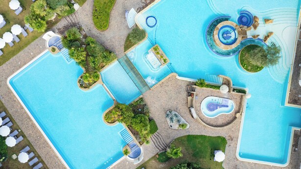 Een groot buitenzwembad met verschillende zones, waaronder een jacuzzi en een glijbaan.