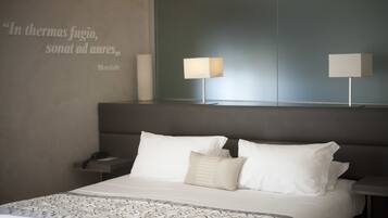 A modern hotel room with a large bed, two bedside lamps, a bedside table, and a wall quote.