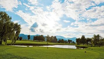 A golf course with a pond, trees, and mountains in the background.