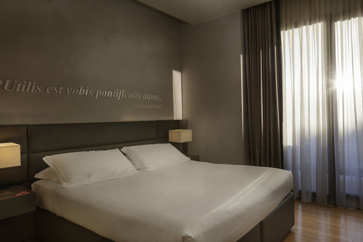 A hotel room with a large bed, two bedside tables, and a wall with a quote.