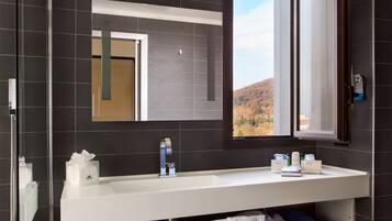 Un baño moderno con un espejo grande, un lavamanos y una ventana que ofrece vistas a un paisaje montañoso.