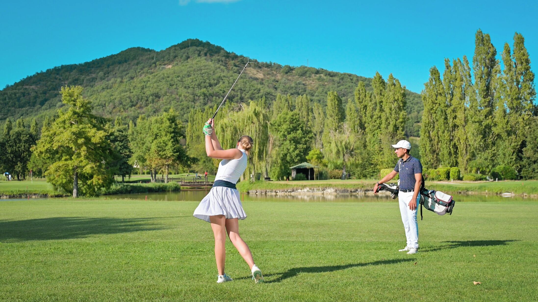 A golf course with a lake, trees, and a mountain in the background.