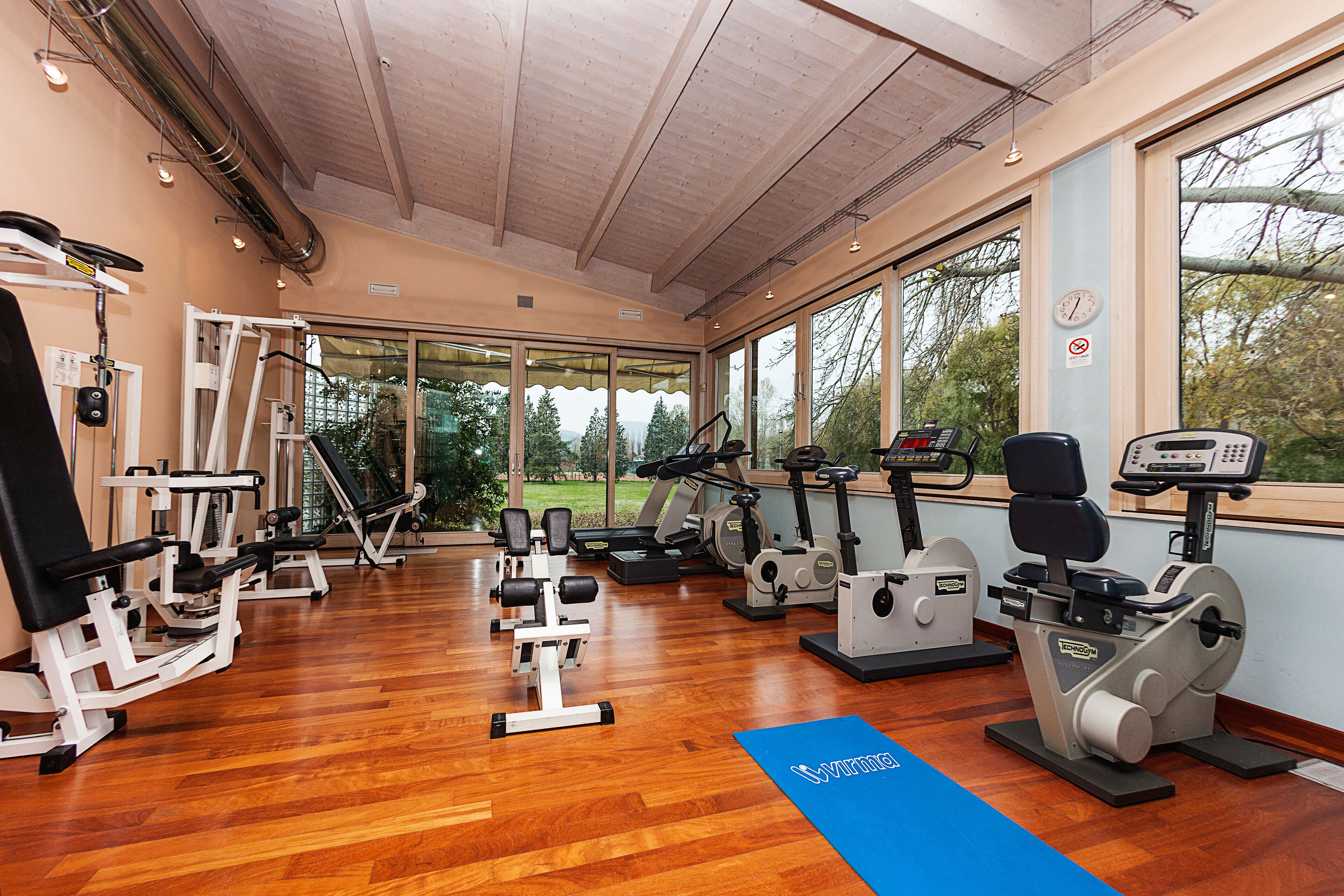 Ein Fitnessstudio mit verschiedenen Trainingsgeräten, großen Fenstern und einer blauen Matte auf dem Boden.