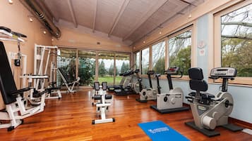 Ein Fitnessstudio mit verschiedenen Trainingsgeräten, großen Fenstern und einer blauen Matte auf dem Boden.