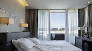 Een moderne hotelkamer met een groot bed, uitzicht op een brug en een bureau met een lamp.