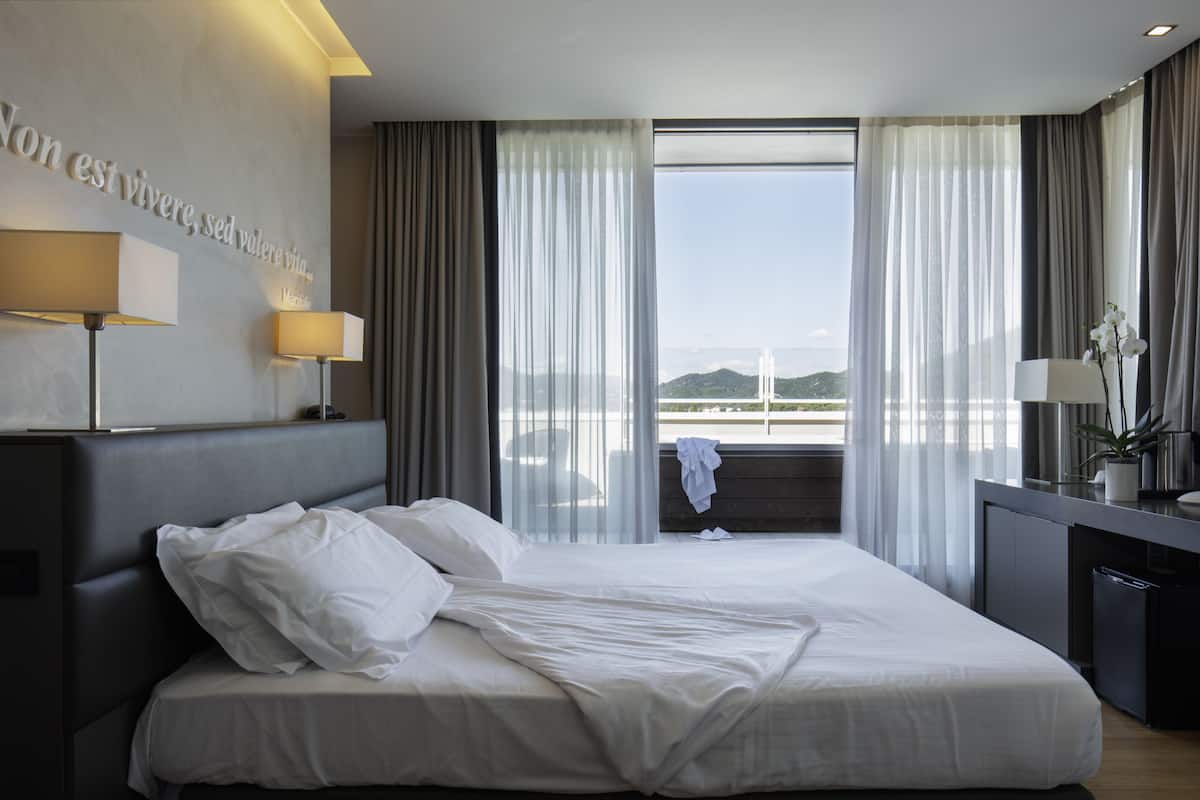 A modern hotel room with a large bed, a view of a bridge, and a desk with a lamp.