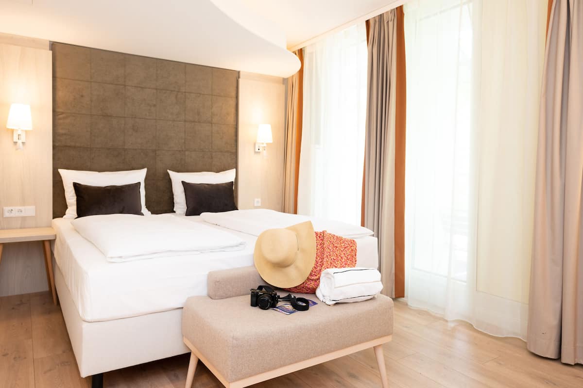 Una habitación de hotel con una cama grande, un espacio de descanso pequeño, una cámara y un sombrero.