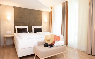 Hotellihuone, jossa on suuri sänky, pieni oleskelualue, kamera ja hattu.