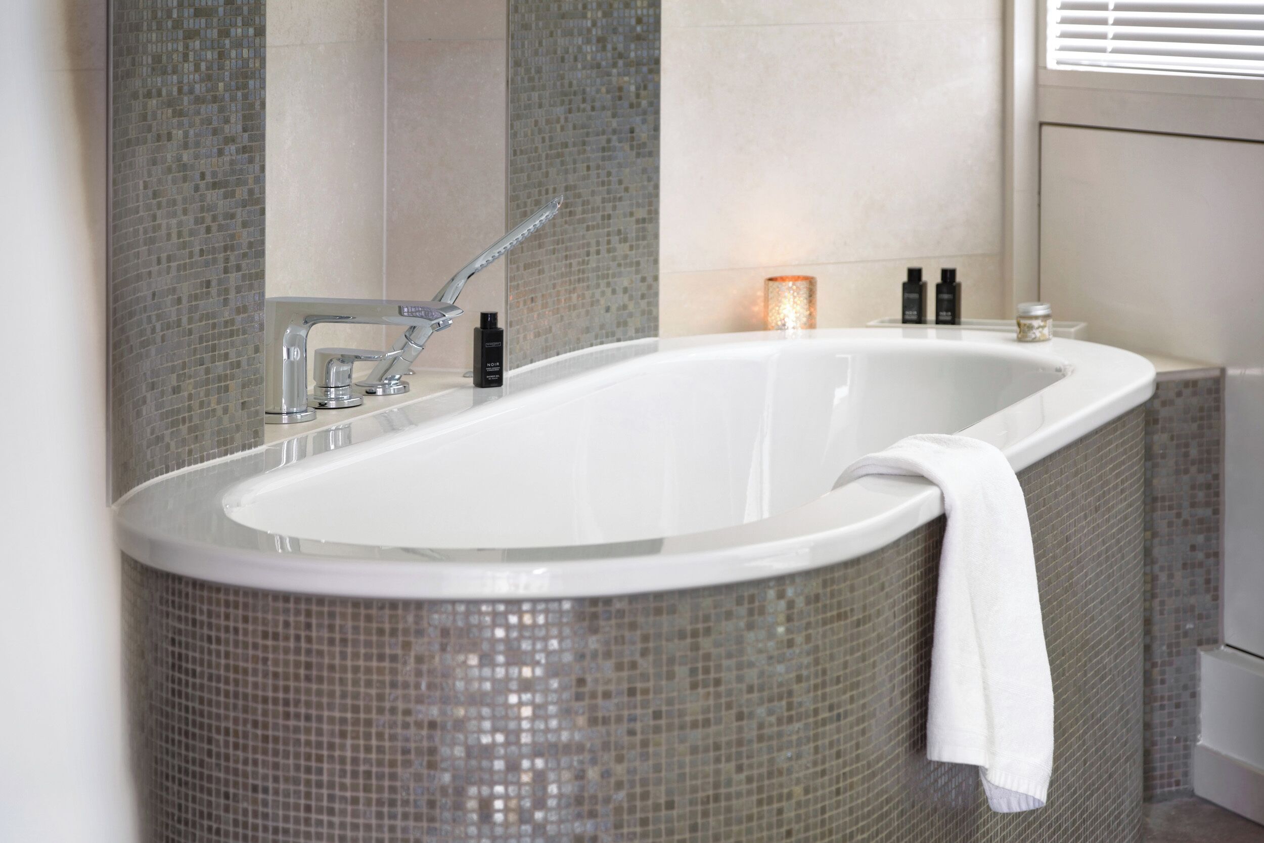 A modern bathroom with a freestanding bathtub, a showerhead, and a mosaic tile wall.