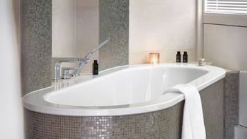 A modern bathroom with a freestanding bathtub, a showerhead, and a mosaic tile wall.
