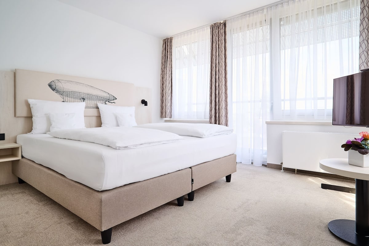 Una habitación de hotel moderna con una cama grande, una mesita de noche, un pequeño escritorio y un televisor.