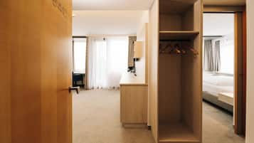 Habitación de hotel con un armario de madera, un escritorio con lámpara, una cama y vistas al exterior a través de una ventana con cortinas.