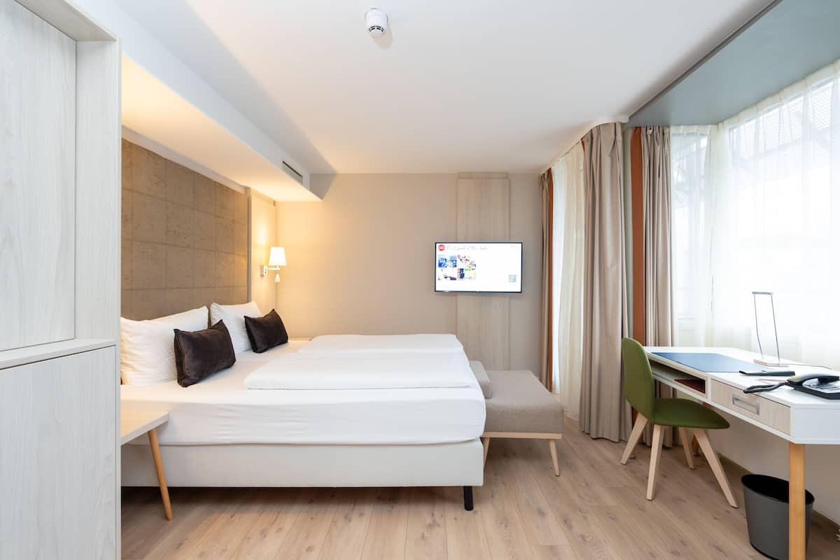Habitación de hotel con cama, escritorio, silla y televisión montada.