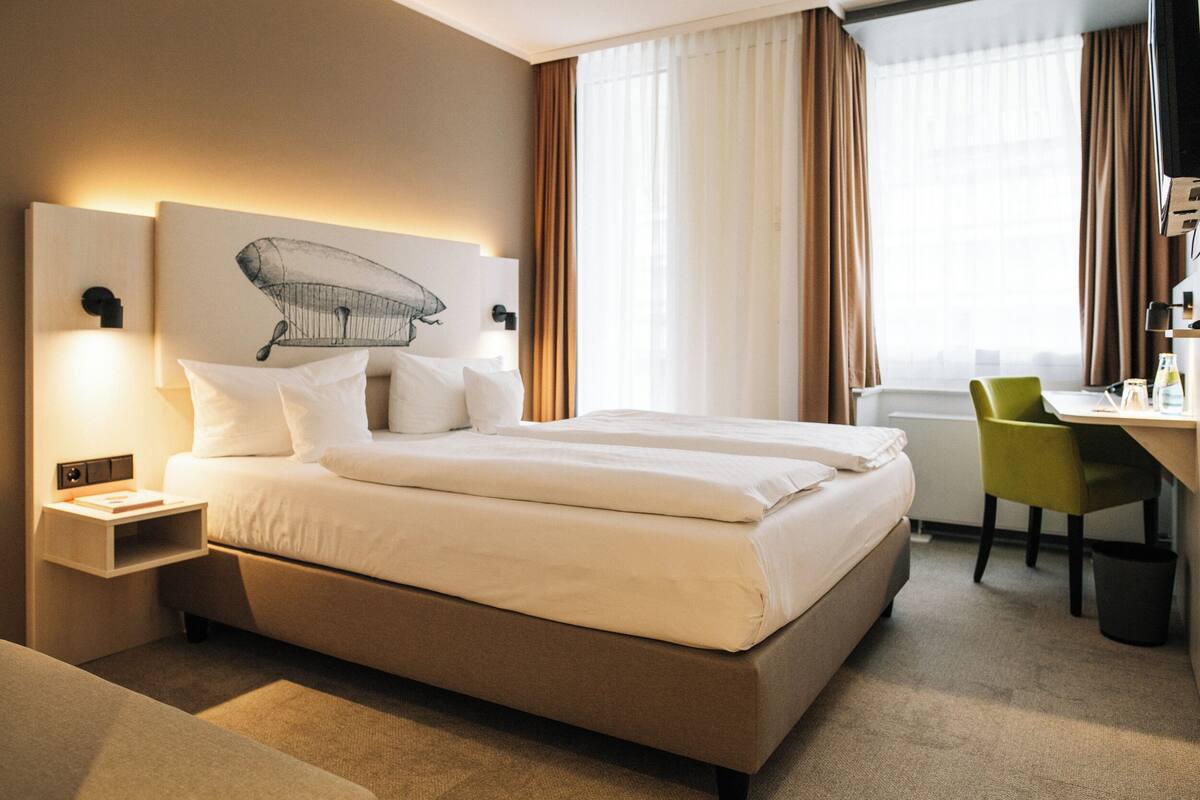 Una habitación de hotel con una cama grande, un escritorio, una silla y una mesita de noche.